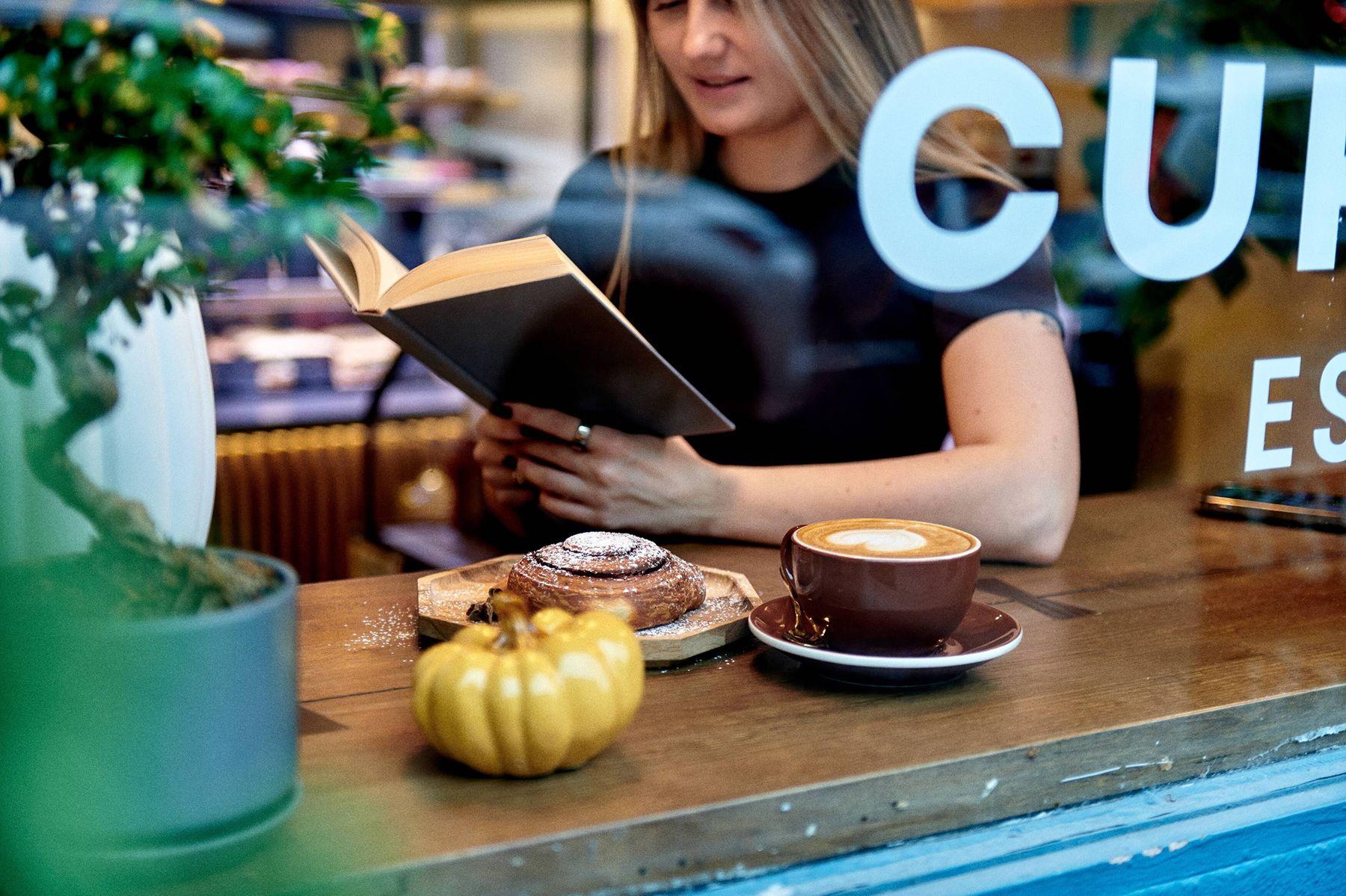 A guest reading a book at the window counter beside a latte and a pastry