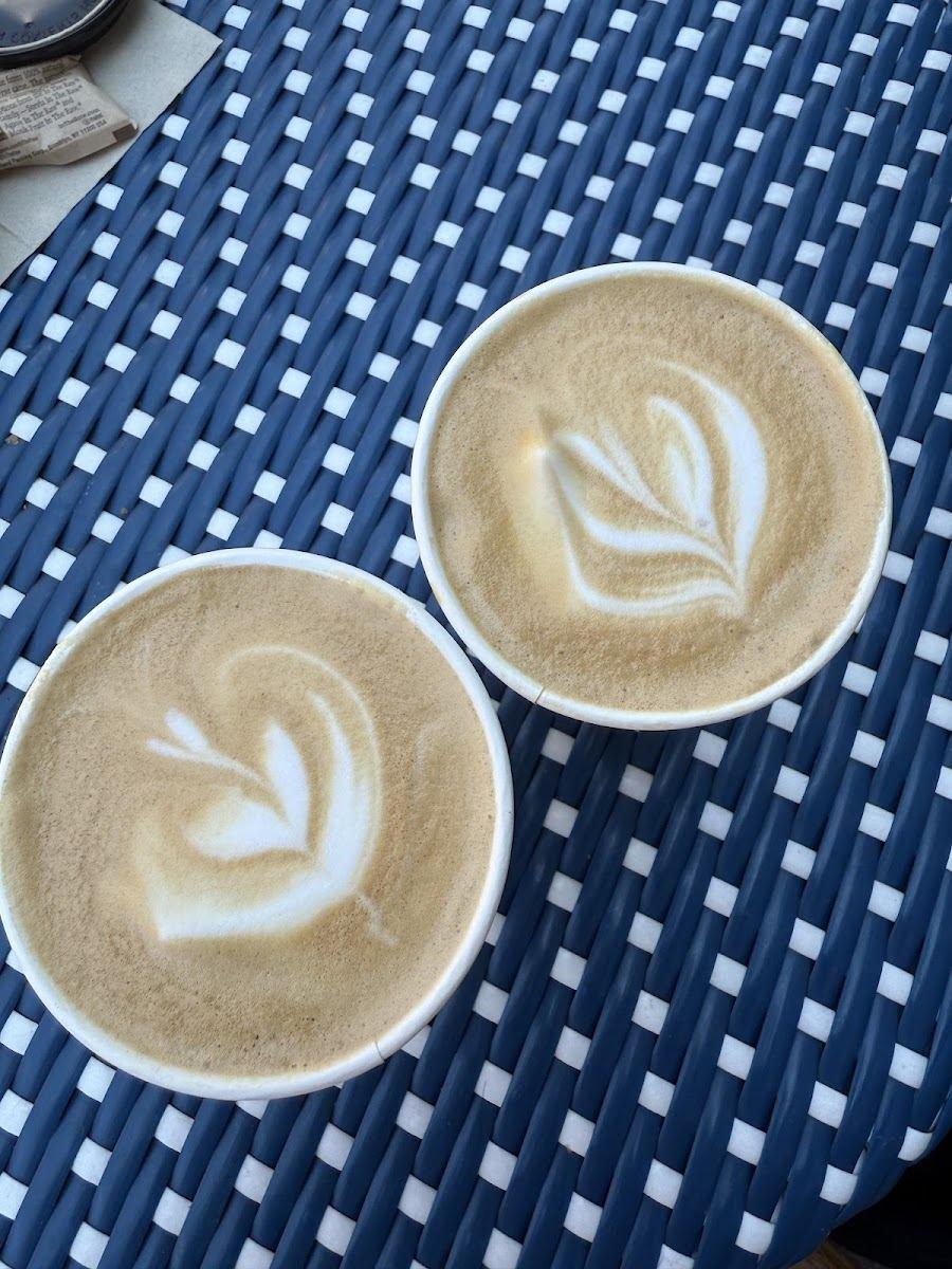 Two lattes with leaf art on a woven café table outside